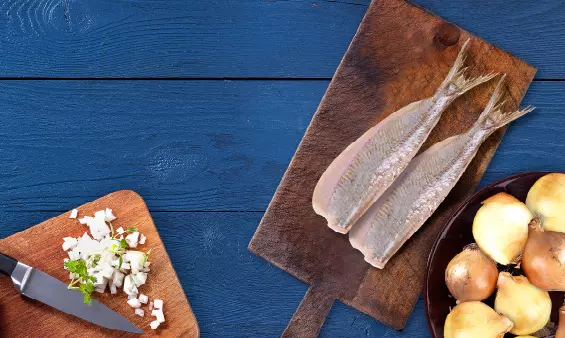 Zwei Heringsfilets ohne Haut auf Holzbrett mit Zwiebeln