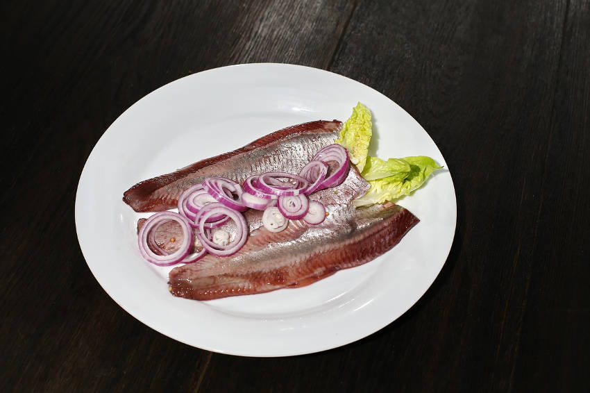 Frischer Hering mit Zwiebeln und Salat auf einem Teller Ein Teller mit frischem Hering, garniert mit roten Zwiebelscheiben und einem Salatblatt, serviert auf dunklem Holztisch