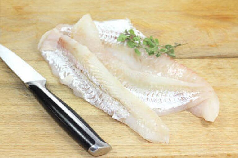 Frischer Fisch auf Schneidebrett mit Messer und Kräutern Frisches Fischfilet auf einem Holzschneidebrett mit einem scharfen Messer und aromatischen Kräutern zur Zubereitung.