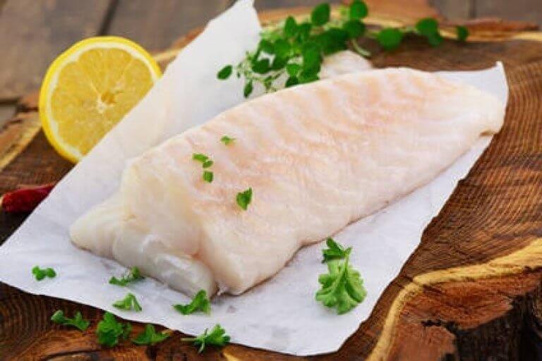 Frisches Fischfilet mit Zitrone und Petersilie auf Holzuntergrund Ein rohes Fischfilet garniert mit Kräutern und einer Zitronenscheibe auf einem Holzbrett, ideal für gesundes Kochen