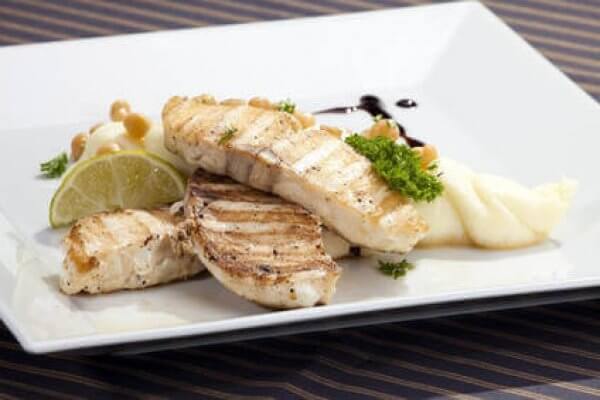 Gegrilltes Fischfilet mit Kartoffelpüree und Limette auf weißem Teller Ein leckeres gegrilltes Fischfilet serviert mit Kartoffelpüree, Limettenscheiben, Kräutern und einer Sauce auf einem weißen Teller.