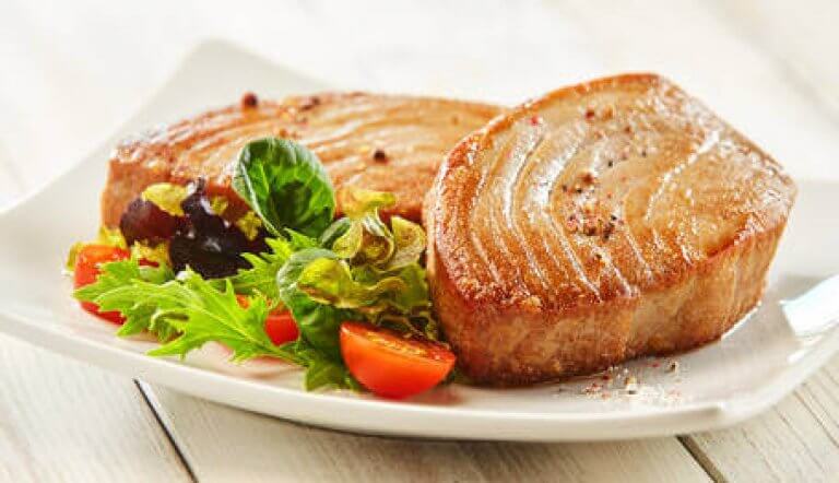 Saftiges Thunfischsteak mit frischem Salat serviert Ein Teller mit zwei Thunfischsteaks und frischem Salat, darunter verschiedene Blattsalate und kleine Tomaten.