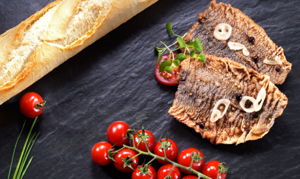 Frisches Baguette mit knusprigem Fisch und Tomaten Ein Baguette, serviert mit knusprigen Fischfilets, Kirschtomaten und frischen Kräutern auf einem dunklen Untergrund
