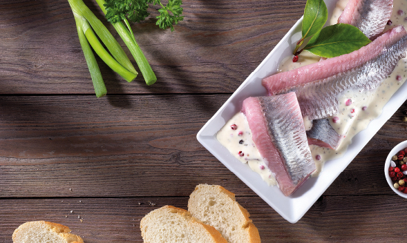 Frische Heringfilets in Sahnesoße mit Baguette und Frühlingszwiebeln Ein Teller mit Heringfilets in Sahnesoße, dekoriert mit Kräutern und serviert mit Baguettescheiben und Frühlingszwiebeln auf einem Holztisch.