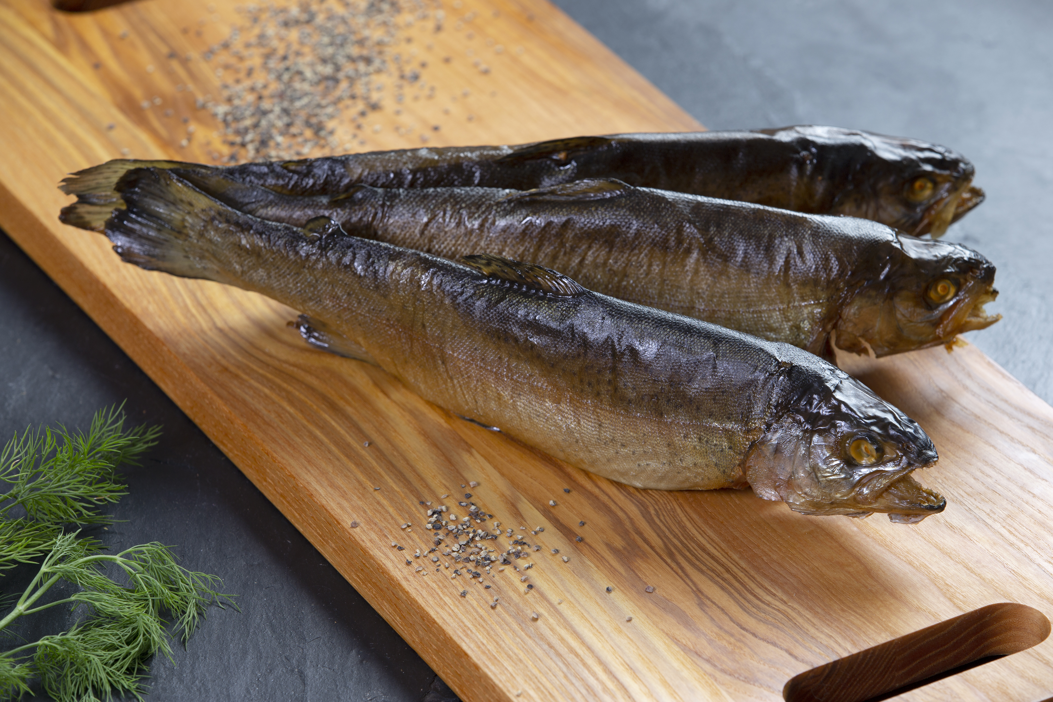 Drei geräucherte Fische auf Holzbrett mit Gewürzen Geräucherte Fische auf einem Holzbrett mit Pfefferkörnern und Dill