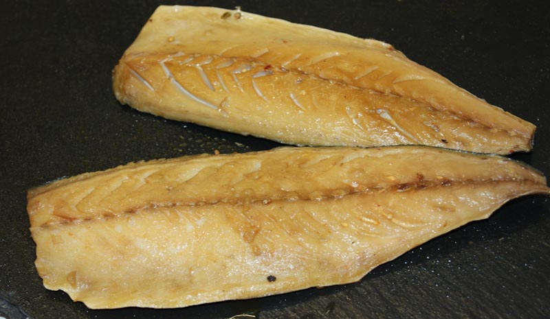Geräucherte Makrelenfilets auf dunklem Hintergrund Zwei geräucherte Makrelenfilets auf einer dunklen Oberfläche liegend, die goldbraun glänzen und eine aromatische Textur haben.