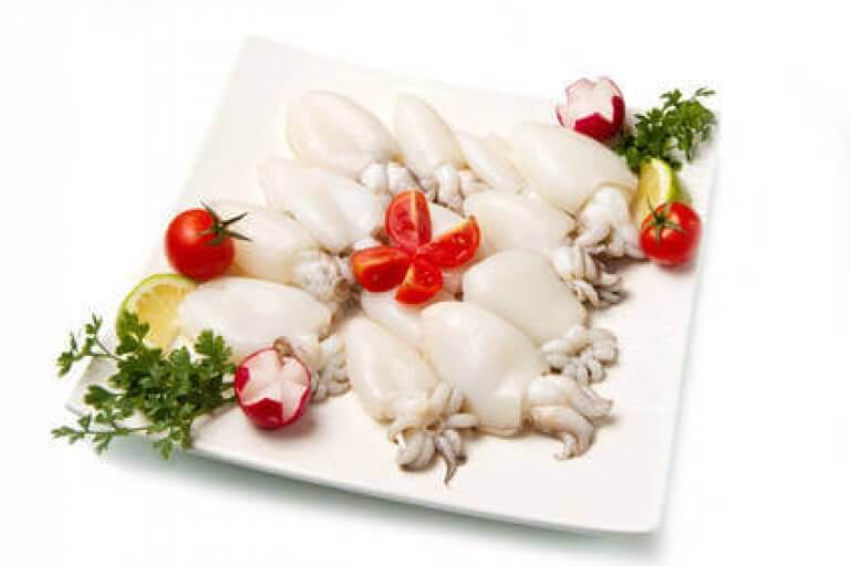 Tintenfischplatte mit Kirschtomaten und Kräutern Eine kunstvoll angerichtete Platte mit Tintenfischen, dekoriert mit Kirschtomaten, Radieschen und frischen Kräutern.