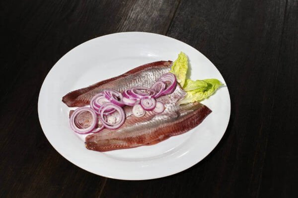 Frischer Matjes mit roten Zwiebeln und Salat auf weißem Teller Matjesfilets garniert mit roten Zwiebelscheiben und grünem Salat auf einem weißen Teller