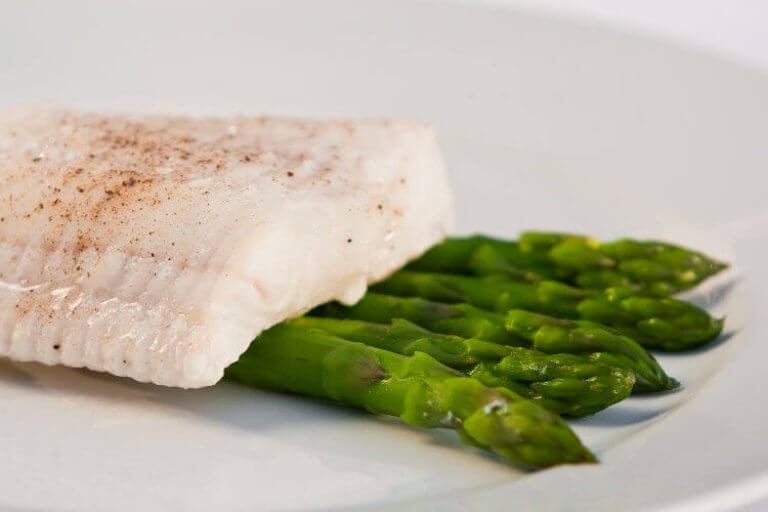 Gedünstetes Fischfilet mit grünem Spargel auf Teller Ein zartes, gedünstetes Fischfilet, serviert mit knackigem grünem Spargel auf einem weißen Teller.
