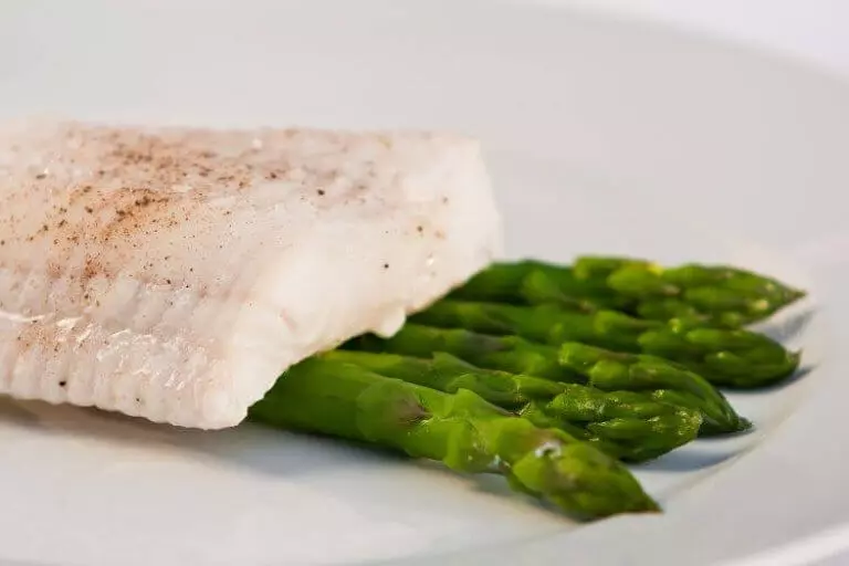 gegartes Kabeljaufilet auf grünem Spargel auf weißem Teller