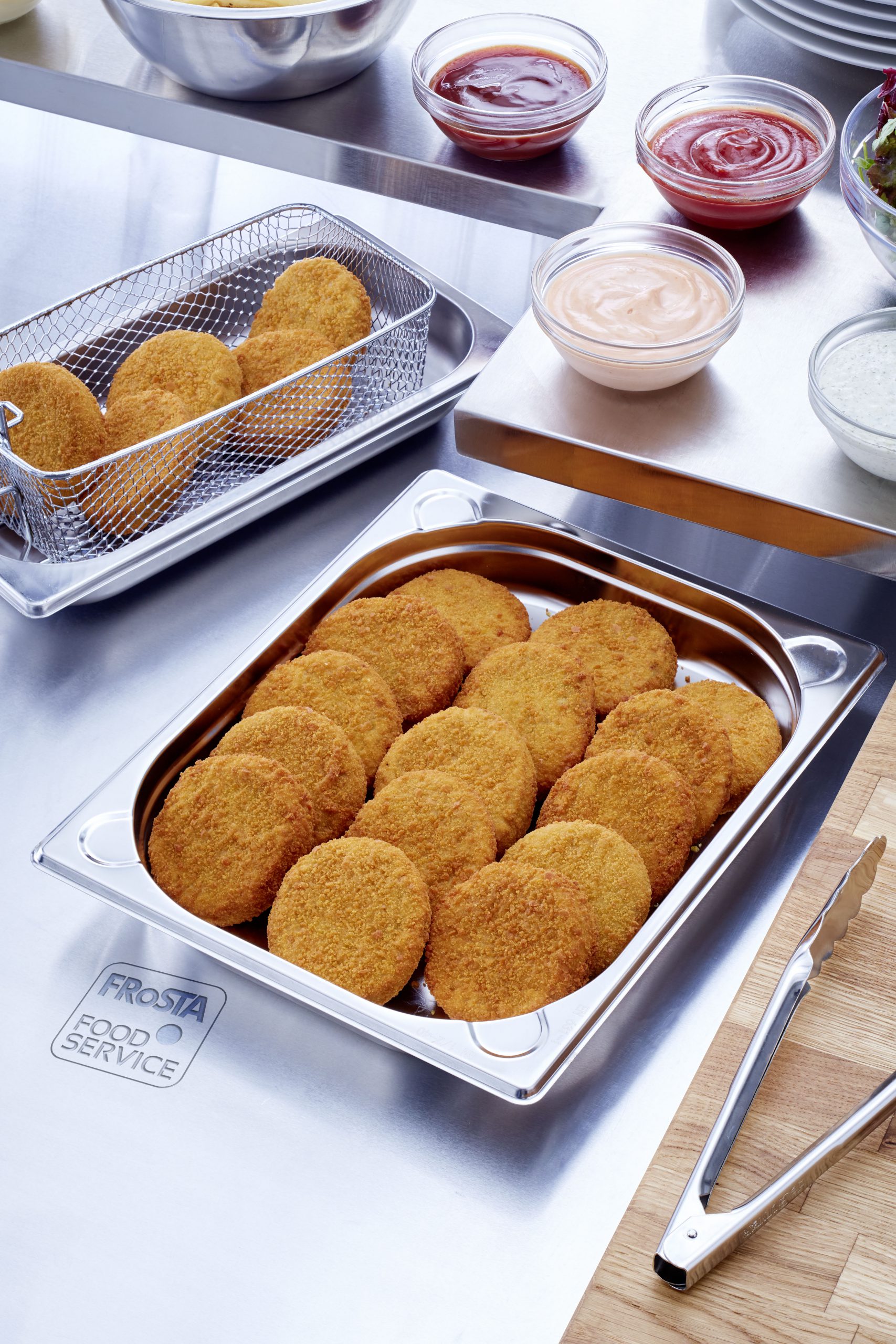 Knusprige Panierprodukte in Edelstahlschale mit Saucen Verschiedene panierte Lebensmittel in Edelstahlschale neben verschiedenen Dips auf einem Tisch