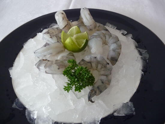 Frische Garnelen auf Eis mit Limette und Petersilie Frische, ungekochte Garnelen auf einem Teller mit Eis, Limettenspalte und Petersilienzweig. Perfekt für Meeresfrüchterezepte.
