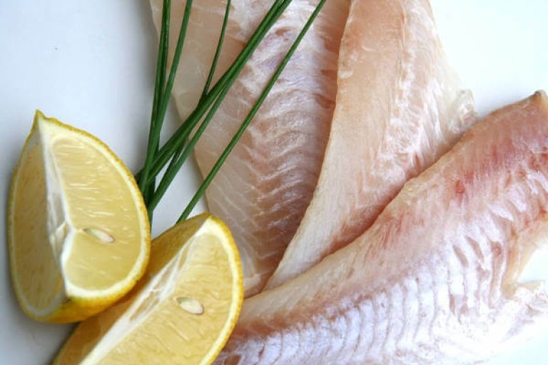 Frische Fischfilets mit Zitrone und Schnittlauch Nahaufnahme von rohen Fischfilets mit Zitronenscheiben und frischem Schnittlauch auf einem weißen Hintergrund