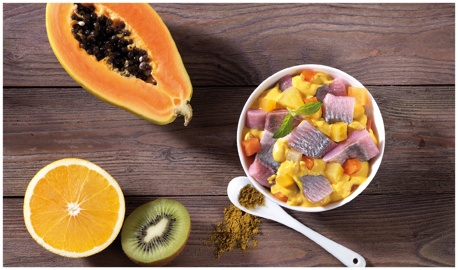 Exotischer Heringssalat mit Papaya und Curry Eine Schale mit Heringssalat, Papaya, Orange, Kiwi und Curry auf einem Holztisch