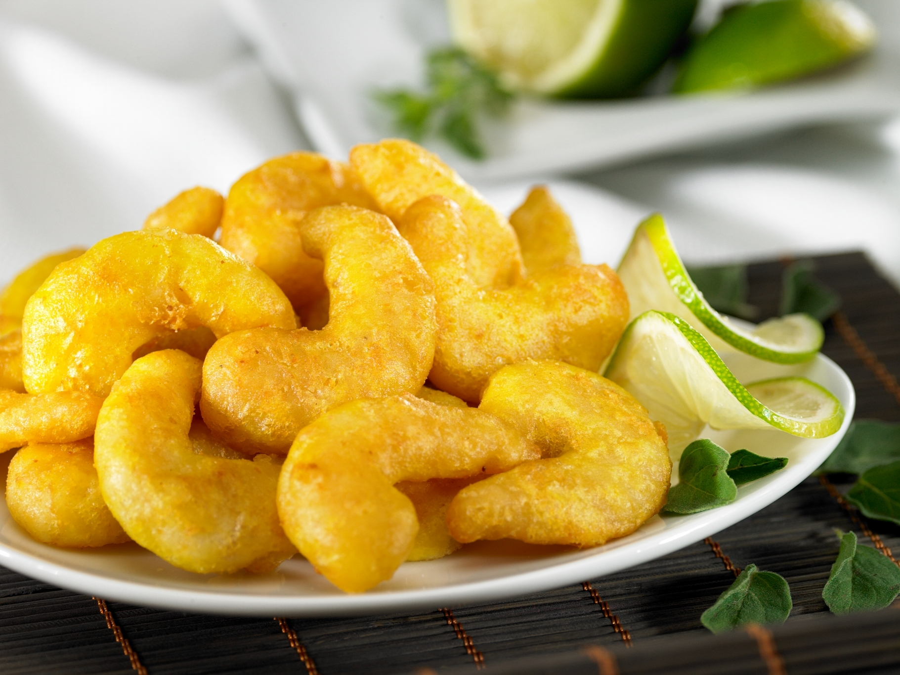 Knusprige frittierte Garnelen mit Limetten-Garnitur Ein Teller mit knusprig frittierten Garnelen, serviert mit frischen Limettenscheiben auf einem dunklen Platzdeckchen.