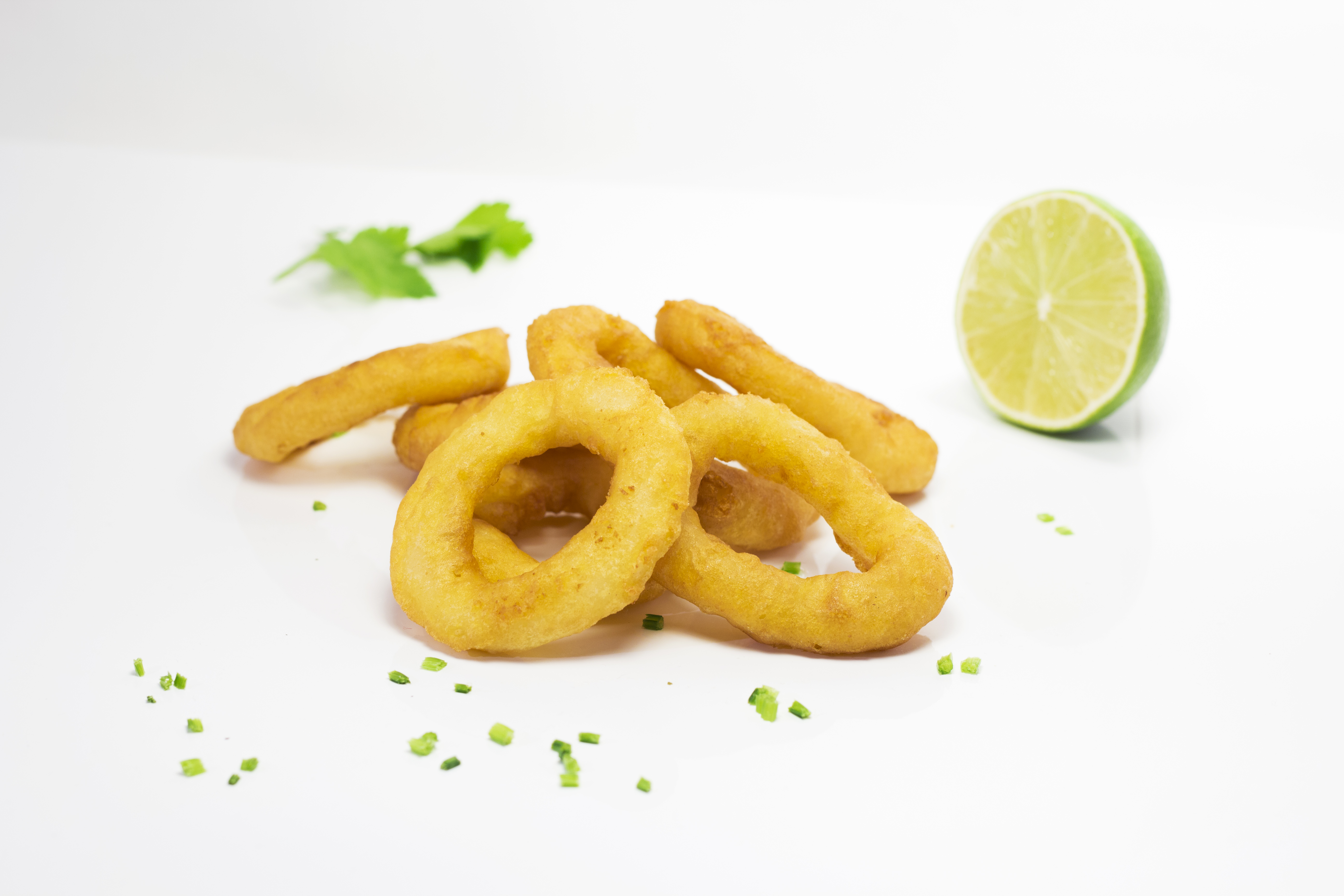 Knusprige Zwiebelringe mit Limettenscheibe und Kräutern garniert Ein Teller mit knusprigen Zwiebelringen, begleitet von einer halben Limette und bestreut mit frischen Kräutern auf weißem Hintergrund