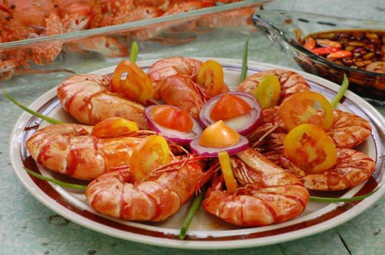 Frisch servierte Garnelen mit Gemüsebeilage Ein Teller mit Garnelen, dekoriert mit Tomaten, Zwiebeln und grünem Gemüse, neben einer Schale Soße.
